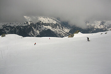 Skiers on a snowy slope with mountains in the background