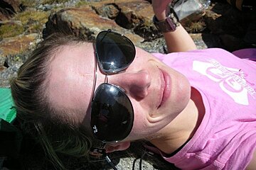 A woman wearing ray-ban sunglasses is laying on a rock