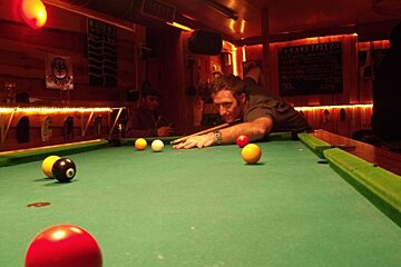 A man is playing pool in a bar with a sign that says beer