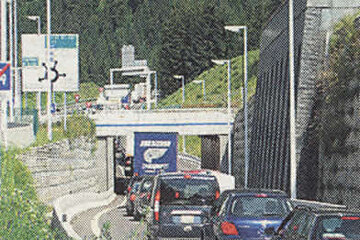 A row of cars are driving down a highway near a tunnel