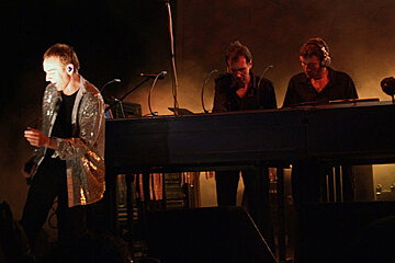 A man in a sequined jacket stands in front of a keyboard