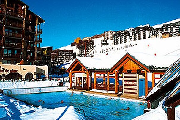 A large swimming pool surrounded by snow with people swimming in it