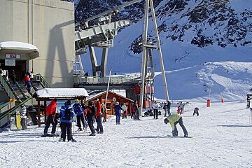 Skiers standing around by lifts up mountain
