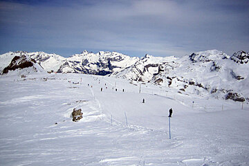 Skiers on a snowy slope with mountains in the background