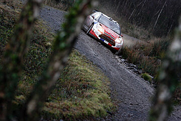 A red and white citroen car is driving down a dirt road