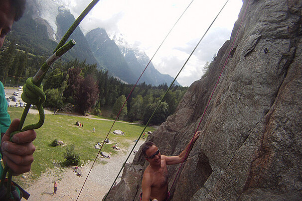 A man climbs a rock wall with mountains in the background