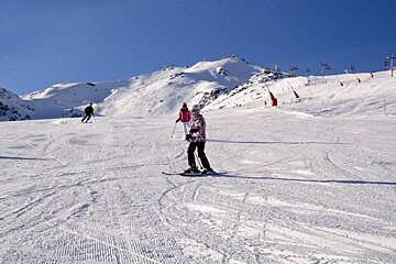 People skiing down a snow covered slope with mountains in the background