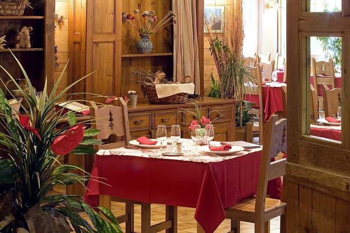 an image of a room with plants and dining tables with red tablecloths on