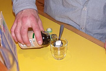 A person pouring liquid into a glass with a spoon