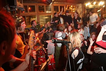 A man playing a guitar in front of a crowd with a woman singing into a microphone