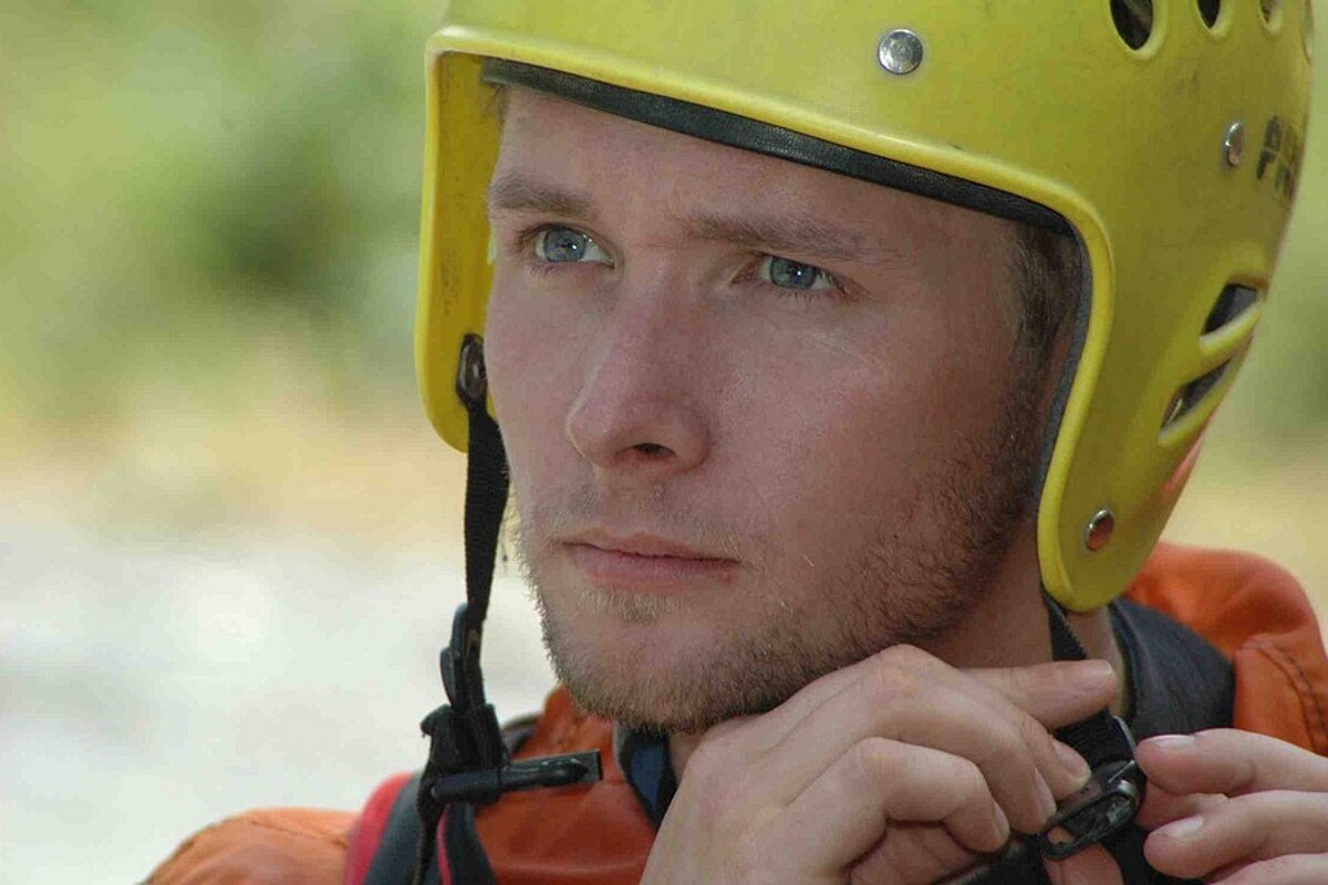 A man wearing a yellow helmet adjusts his strap