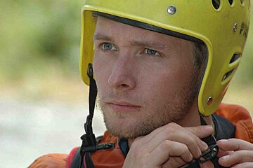 A man wearing a yellow helmet adjusts his strap