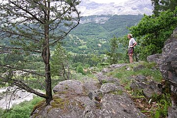 A man stands on a rocky cliff overlooking a mountain valley