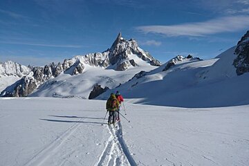 Two people skiing down a snowy slope with mountains in the background
