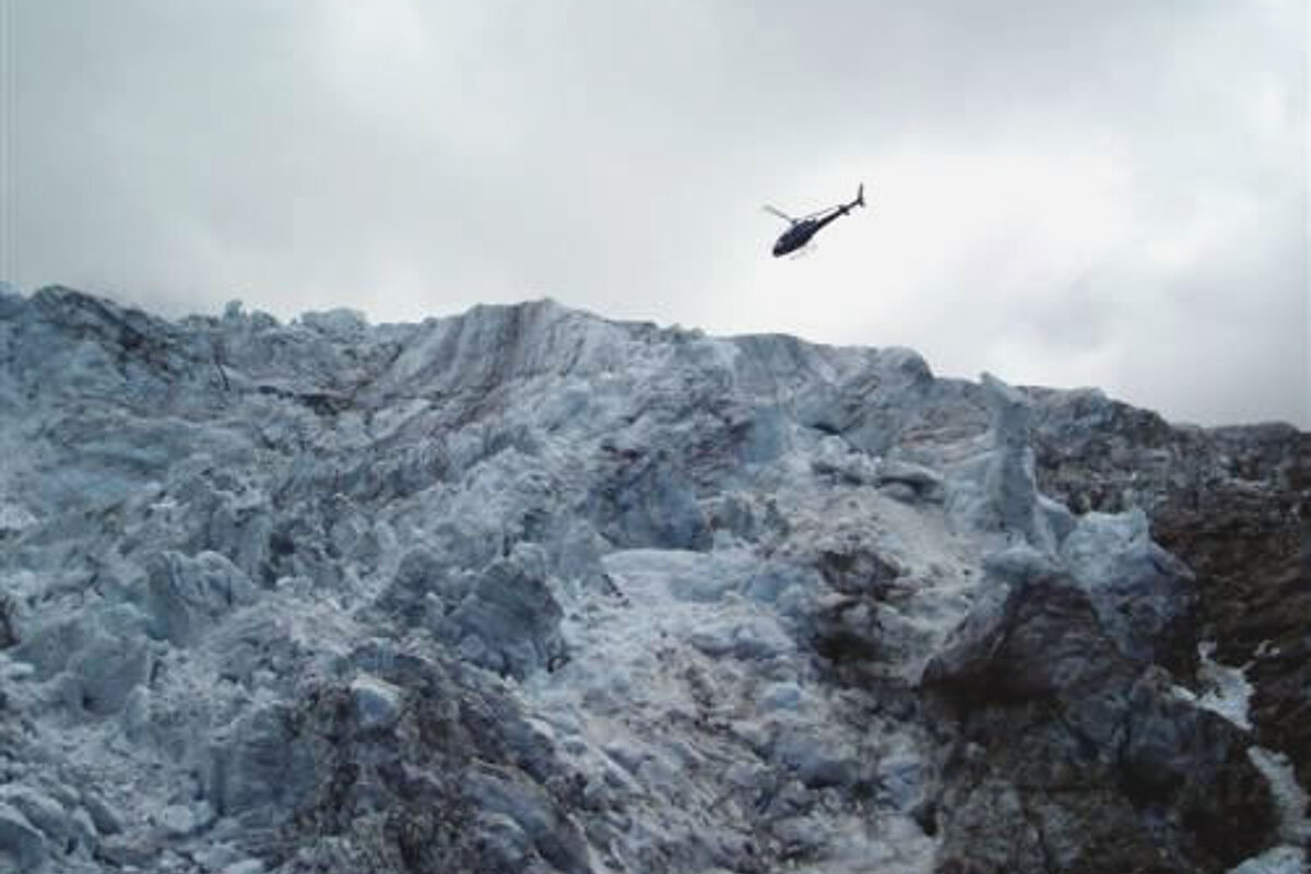 A helicopter is flying over a large snow covered mountain