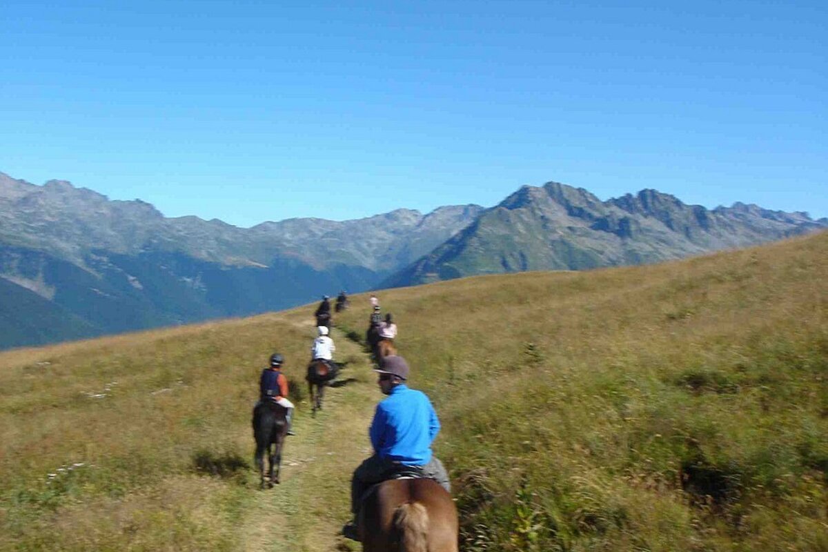A group of people riding horses in a field with mountains in the background