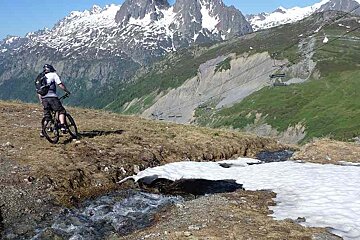 an image of a snow bridge over a stream with a man mountain biking
