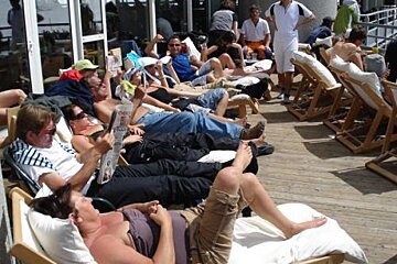 A group of people are laying on a deck reading newspapers