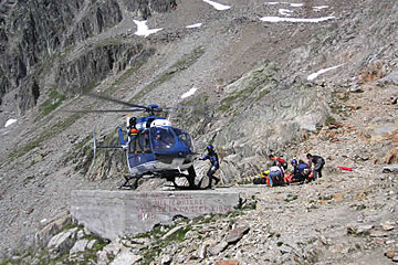 A blue helicopter is landing on a rocky hillside