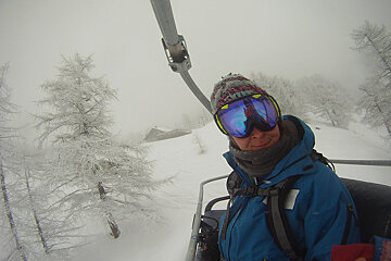 A person wearing a blue jacket and goggles is riding a ski lift