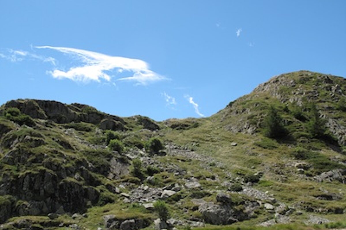 A mountain covered in grass and rocks with a blue sky in the background