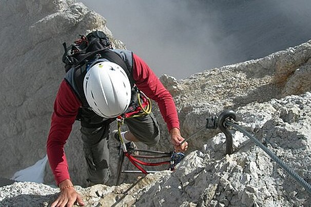 A person wearing a white helmet is climbing a rocky mountain