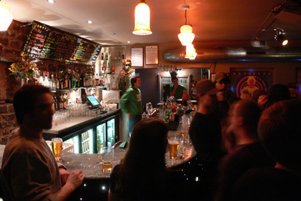 A crowd of people are gathered at a bar with a menu on the wall