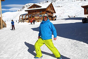 A man in a blue jacket and yellow pants stands on a snowy slope