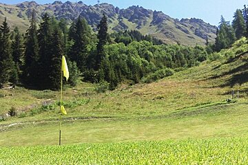 A yellow flag on a golf course with mountains in the background
