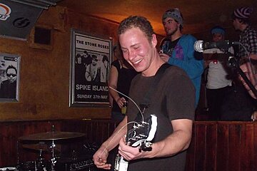 A man playing a guitar in front of a spike island poster