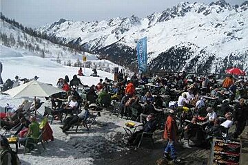 A large group of people are sitting at tables and chairs on top of a snow covered mountain