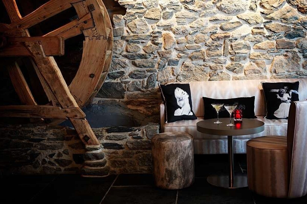 an image of a water wheel on a stone wall next to a bar table and stools