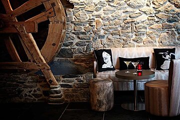 an image of a water wheel on a stone wall next to a bar table and stools