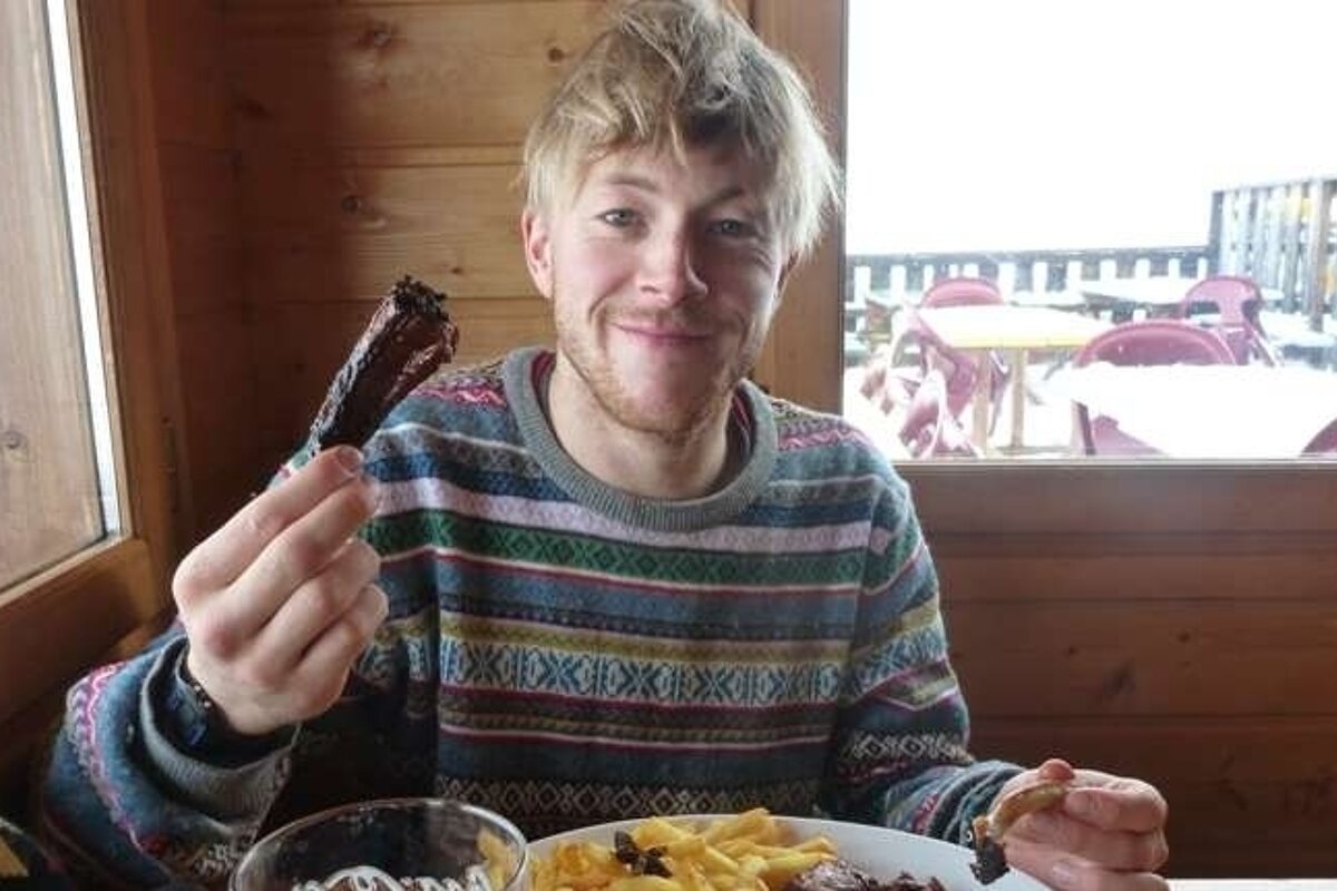 A man in a colorful sweater is eating ribs and french fries