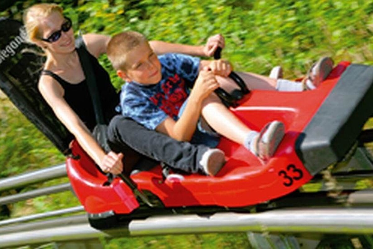 an image of a woman and a boy sat on an open roller-coaster luge