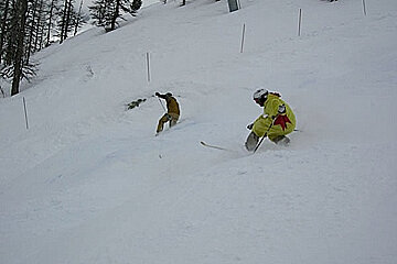 A man in a yellow jacket with a red star on the back is skiing down a snowy hill