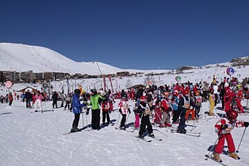 A group of skiers are gathered on a snowy slope with a sign that says ' a ' on it