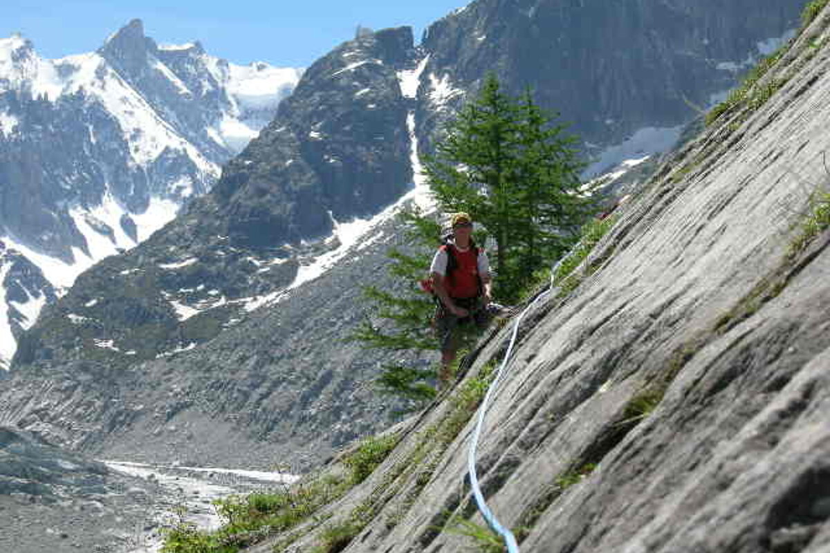 A man is standing on a rocky cliff with mountains in the background