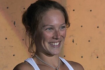 A woman wearing a white tank top and a necklace smiles