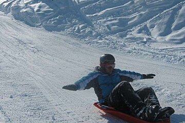 A person sledding down a snowy hill with their arms outstretched