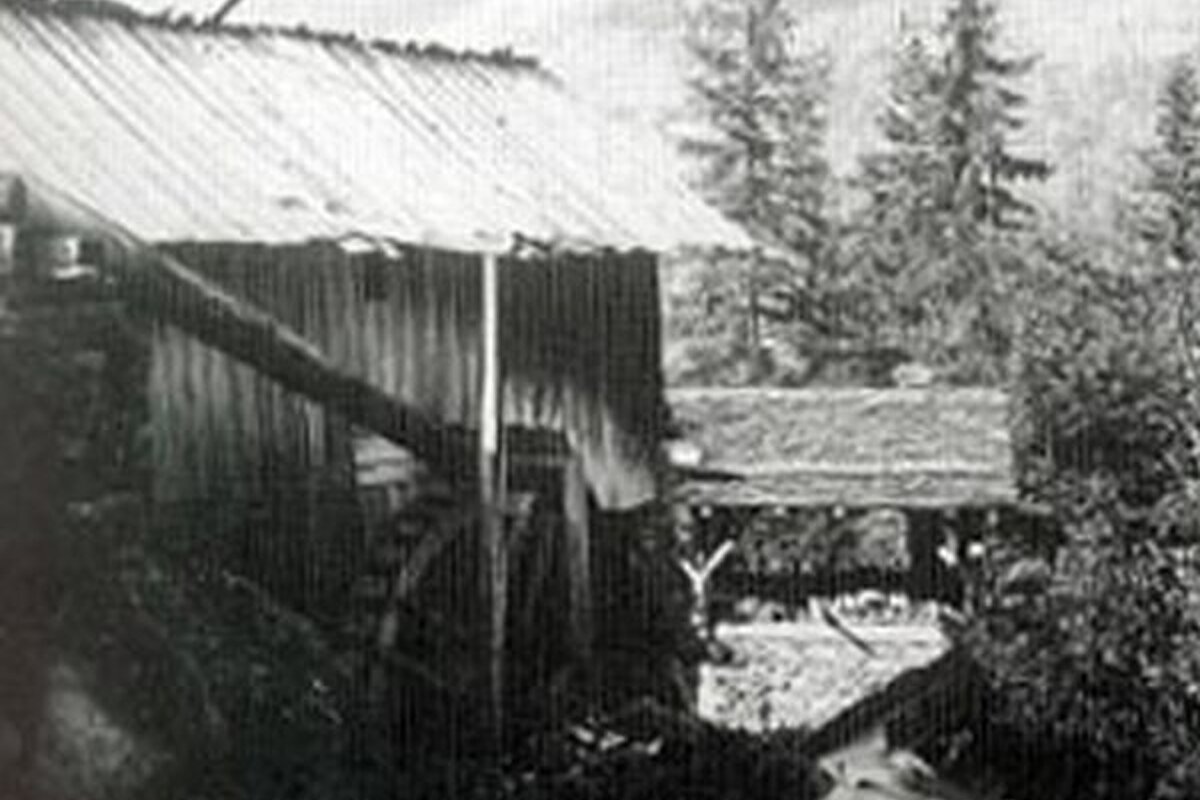 A black and white photo of a wooden building next to a river