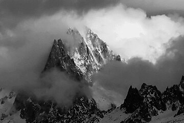 A black and white photo of a mountain covered in snow and clouds