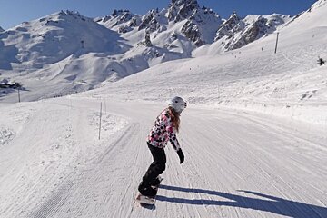A woman is snowboarding down a snowy slope with mountains in the background
