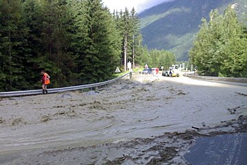 A man in a red jacket stands on a flooded road
