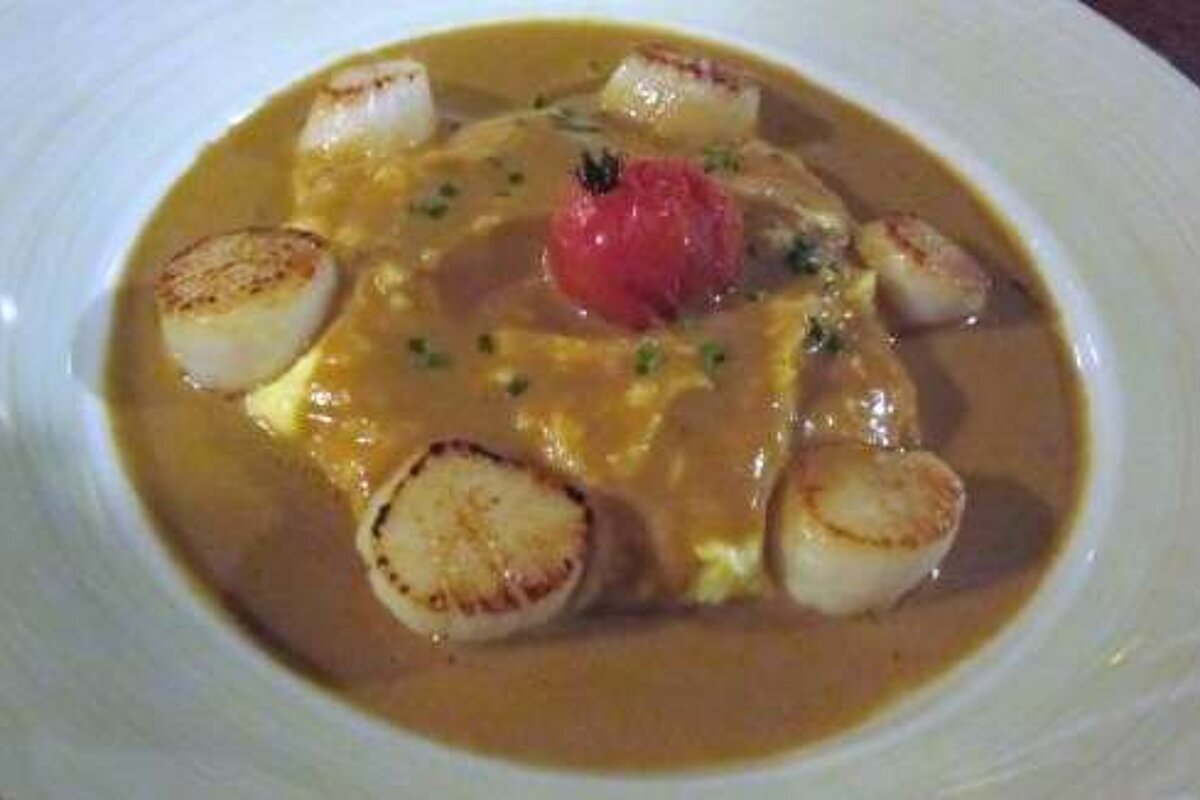 A close up of a plate of food with scallops and a tomato on top