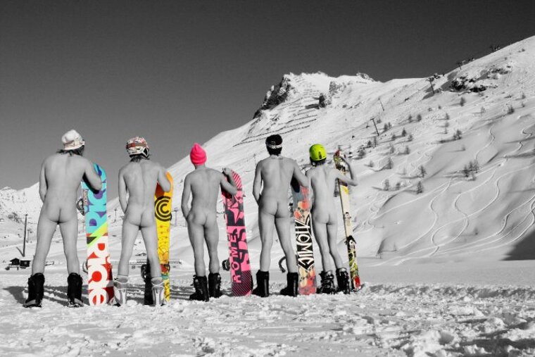 A group of men standing in the snow holding snowboards one of which says atomic on it