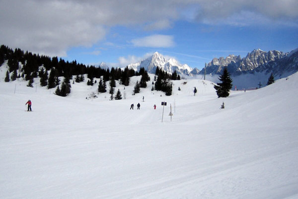 People skiing down a snowy slope with mountains in the background