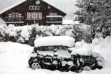 A car is covered in snow in front of a house