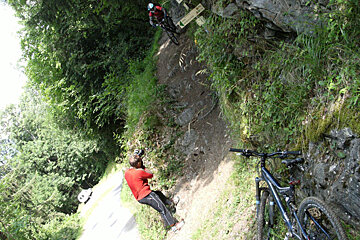 A man in a red shirt is taking a picture of a person on a bike