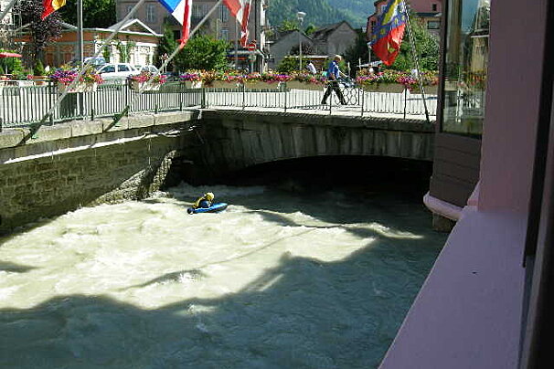 A man in a kayak is going down a river under a bridge